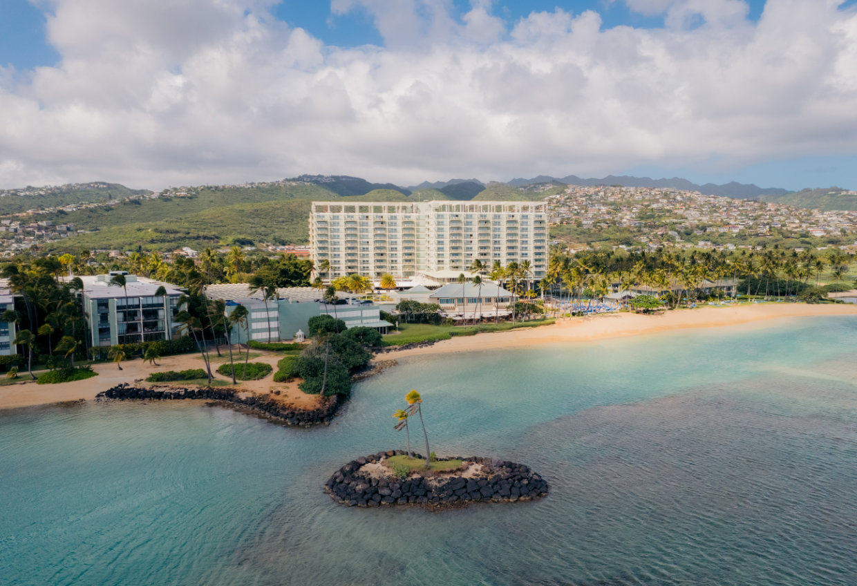 Aerial view of a beachfront hotel with a mountainous backdrop and ocean view.